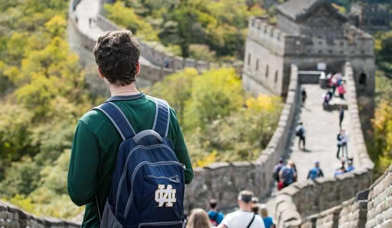 A student with a Notre Dame backpack stands on the Great Wall of China.